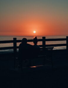 people sitting on a bench at sunset