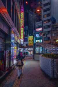 a woman walking down a sidewalk in a city at night
