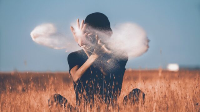 man sitting on brown grass field playing with smoke