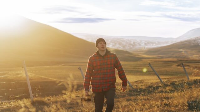 a man is walking through a field with mountains in the background